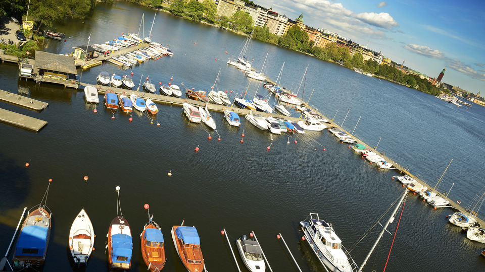 En småbåtshamn från ovan. Ett flertal båtar ligger förtöjda vid fyra bryggor. I bakgrunden syns bostäder på Norr Mälarstrand.