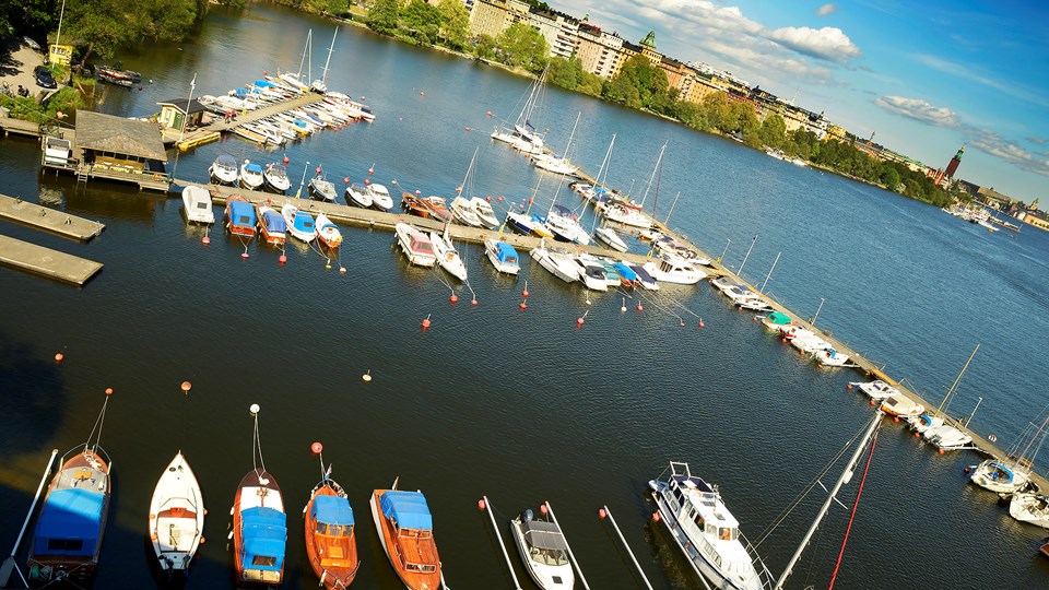 En småbåtshamn från ovan. Ett flertal båtar ligger förtöjda vid fyra bryggor. I bakgrunden syns bostäder på Norr Mälarstrand.